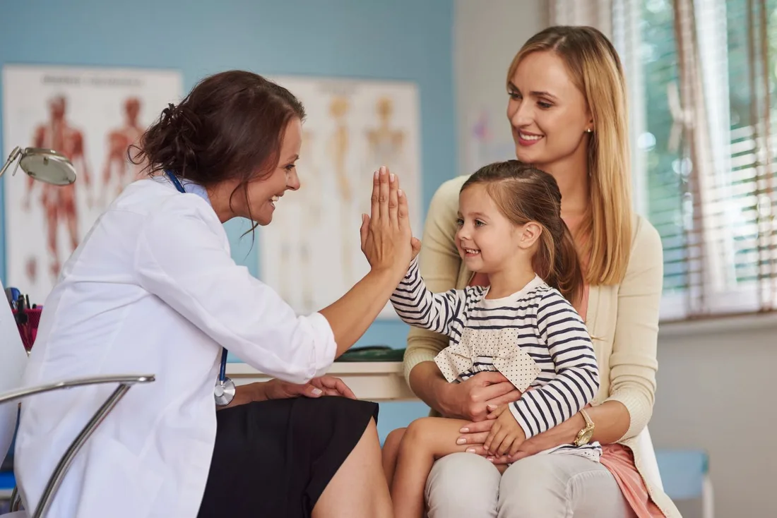 A pediatrician greeting a young patient while a parent looks on